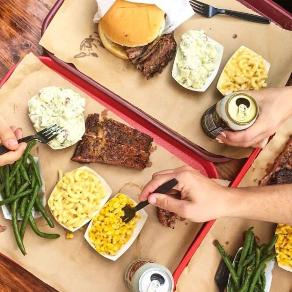 overhead view of people reaching in to eat potato salad, macaroni and cheese and Texas style BBQ