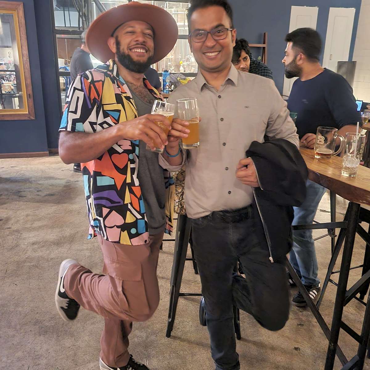 Two people standing in a flamingo pose with beer pints in hand
