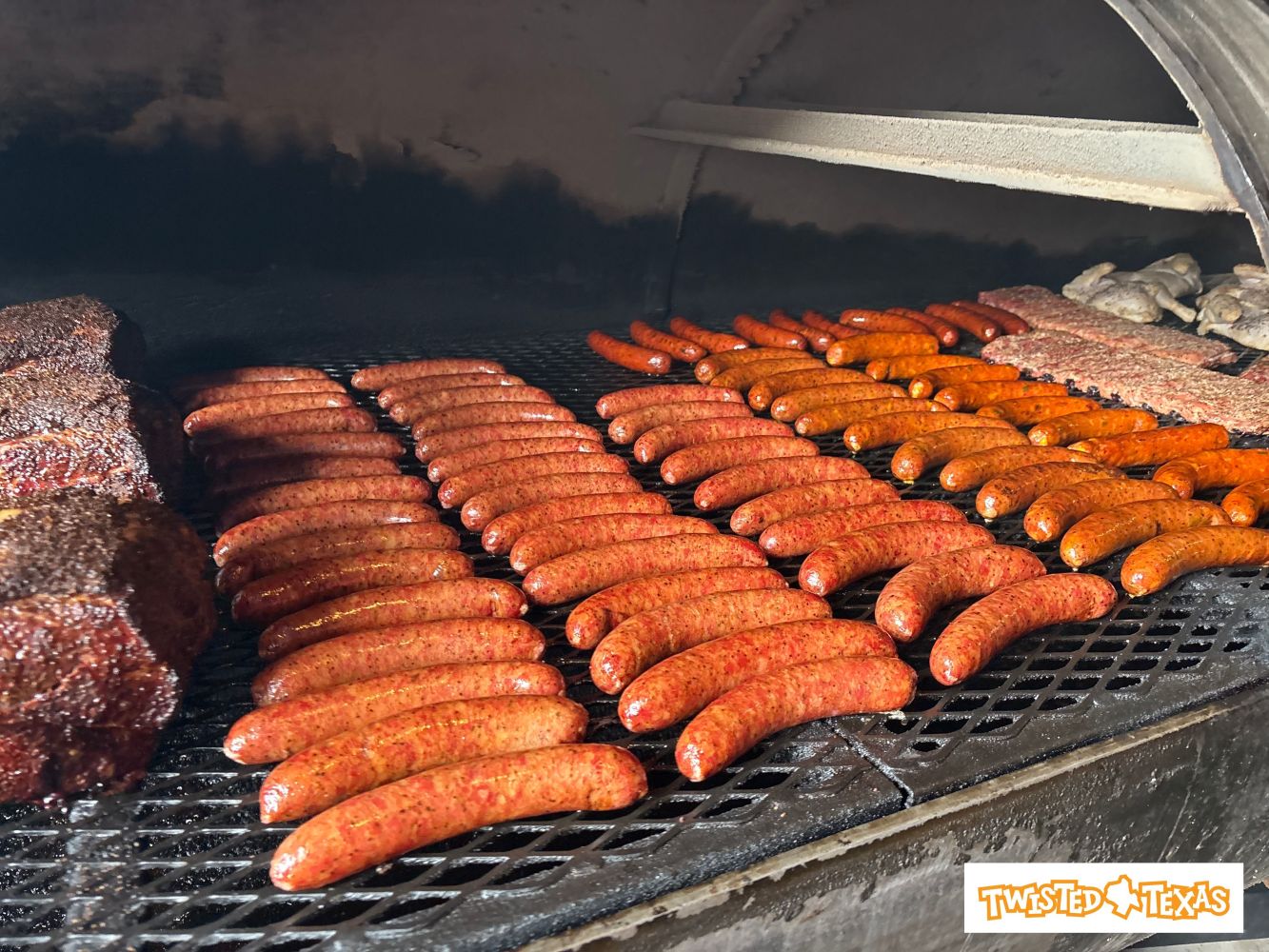 Rows of sausages and meat on a barbecue grill inside a smoker.
