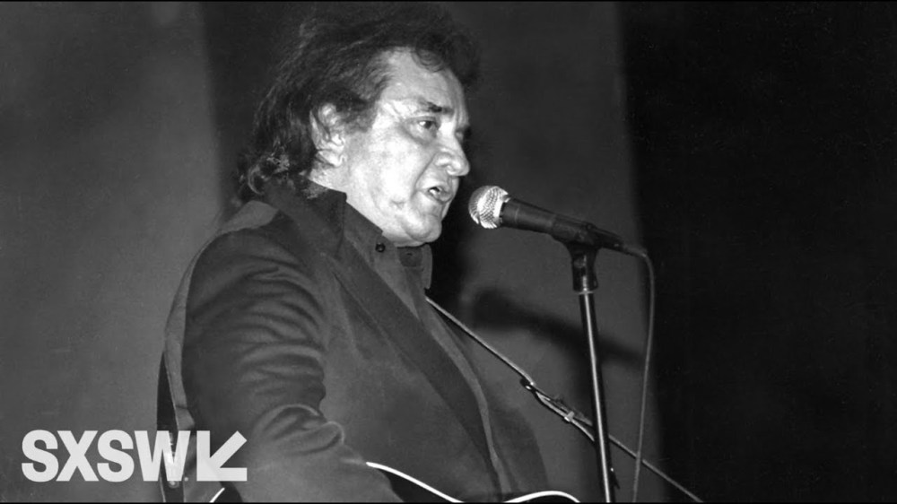 Black and white photo of a man singing into a microphone with 'SXSW' logo in the corner.