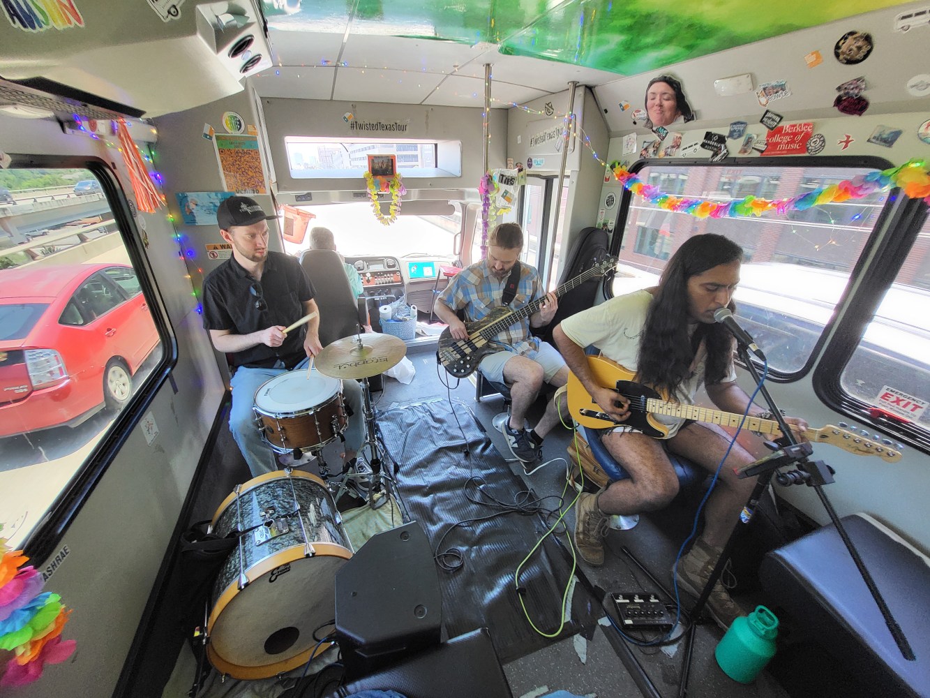 Band performing inside a decorated vehicle with drums, guitar, and bass.